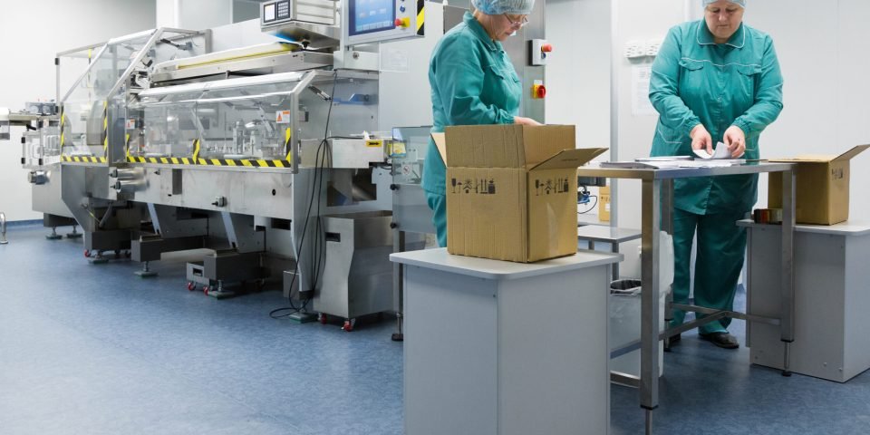 Pharmaceutical technicians work in sterile working conditions at pharmaceutical factory. Scientists wearing protective clothing